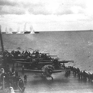 Planes on deck with a vessel taking heavy fire in the background
