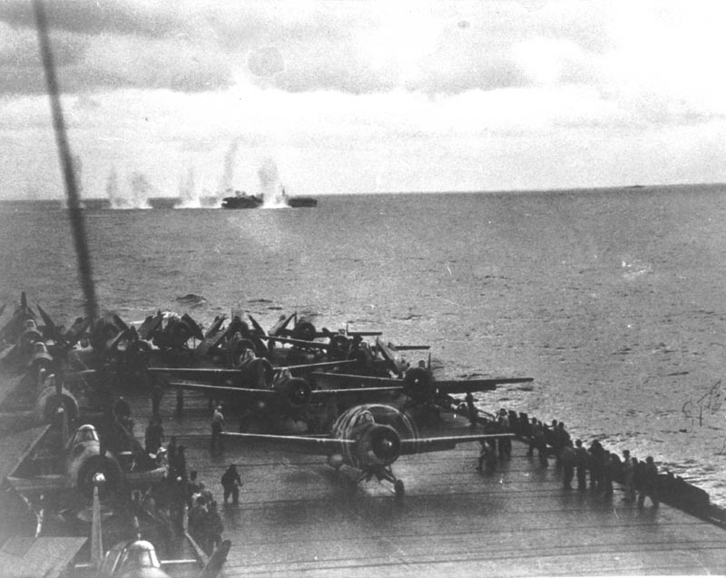 Planes on deck with a vessel taking heavy fire in the background